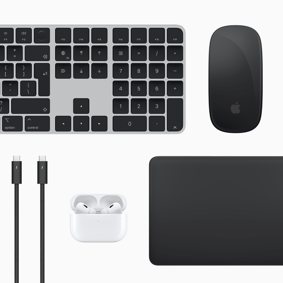 Pohled shora na doplňky k Macu: Magic Keyboard, Magic Mouse, Magic Trackpad, AirPods a Thunderbolt kabely